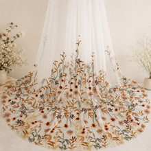 Load image into Gallery viewer, a white veil with a floral pattern, hanging on a stand. The veil is adorned with a variety of flowers in different colors, creating a visually appealing and intricate design. The floral pattern on the veil is detailed and detailed, showcasing the craftsmanship and artistry involved in creating such a piece of clothing.