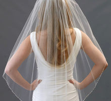 Load image into Gallery viewer, A woman wearing a white wedding dress with a veil stands with her hands on her hips, facing away from the camera.