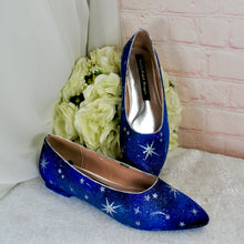 Load image into Gallery viewer, A pair of blue shoes with white star patterns, placed on a white surface next to a bouquet of white flowers.
