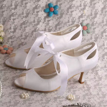 Load image into Gallery viewer, A pair of white high-heeled shoes with bows tied around the toe, placed on a lace background with small flowers and pearls.