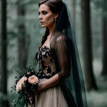 Load image into Gallery viewer, A woman in a black lace dress stands in a forest, holding a bouquet of flowers.