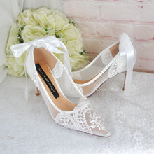 Load image into Gallery viewer, A pair of white lace wedding shoes with a bow on the back, placed on a white surface next to a bouquet of white flowers.