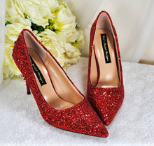 Load image into Gallery viewer, A pair of red glitter high-heeled shoes with a white floral bouquet in the background.
