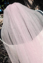 Load image into Gallery viewer, A close-up view of a delicate, pink, sheer veil with a sparkly texture, hanging from a mannequin or a similar structure.