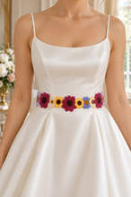Load image into Gallery viewer, A close-up of a woman wearing a white satin spaghetti-strap dress with a colorful crocheted flower belt featuring burgundy, yellow, and blue flowers.