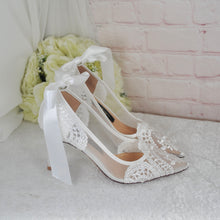 Load image into Gallery viewer, A pair of white lace wedding shoes with bows, placed on a white surface next to a bouquet of white flowers.