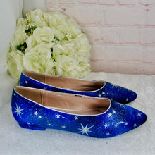 Load image into Gallery viewer, A pair of blue shoes with a starry design, placed next to a bouquet of white flowers against a pink brick wall.