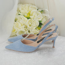 Load image into Gallery viewer, A pair of light blue high-heeled shoes with a clear strap, placed on a white surface next to a bouquet of white roses.