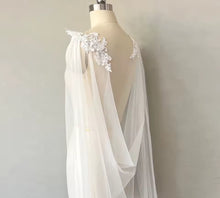 Load image into Gallery viewer, A mannequin wearing a white wedding dress with a sheer, flowing cape-like design and delicate floral accents.
