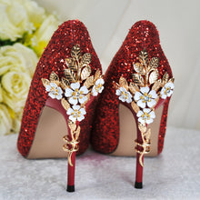 Load image into Gallery viewer, A pair of red high-heeled shoes with gold floral embellishments, placed on a white surface.
