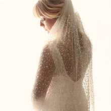 Load image into Gallery viewer, A woman wearing a white wedding dress with a veil, standing in a dimly lit room.
