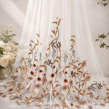 Load image into Gallery viewer, a white sheer curtain with a floral pattern of orange and brown flowers and leaves, hanging on a wall.
