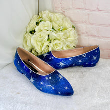 Load image into Gallery viewer, A pair of blue star-patterned shoes with white stars sits on a white surface, accompanied by a bouquet of white flowers.
