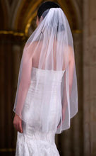 Load image into Gallery viewer, A bride wearing a white wedding dress with a long, flowing veil stands in front of an ornate archway.
