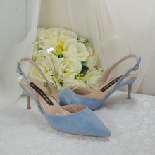Load image into Gallery viewer, A pair of blue high-heeled shoes with a clear strap, placed on a white surface next to a bouquet of white flowers.
