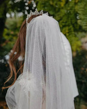 Load image into Gallery viewer, A bride wearing a white veil with a sparkling tiara stands in a lush green garden.
