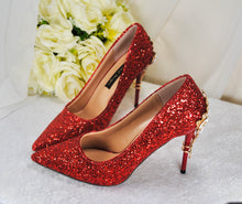 Load image into Gallery viewer, A pair of red glitter high-heeled shoes with a white flower bouquet in the background.
