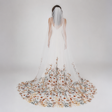 Load image into Gallery viewer, A woman wearing a white wedding dress with a long, flowing veil decorated with floral patterns.
