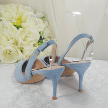 Load image into Gallery viewer, A pair of light blue high-heeled shoes with a clear strap, placed on a white surface with a bouquet of white roses in the background.
