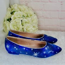 Load image into Gallery viewer, A pair of blue shoes with a starry design, placed next to a bouquet of white flowers against a pink brick wall.
