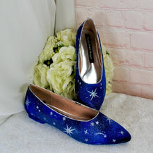 Load image into Gallery viewer, A pair of blue shoes with white star patterns, placed on a white surface next to a bouquet of white flowers.
