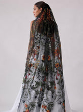 Load image into Gallery viewer, A woman shown from the back wearing a sheer black embroidered cape with a long matching veil, featuring floral and botanical patterns in orange, green, and brown on a light gray studio background.
